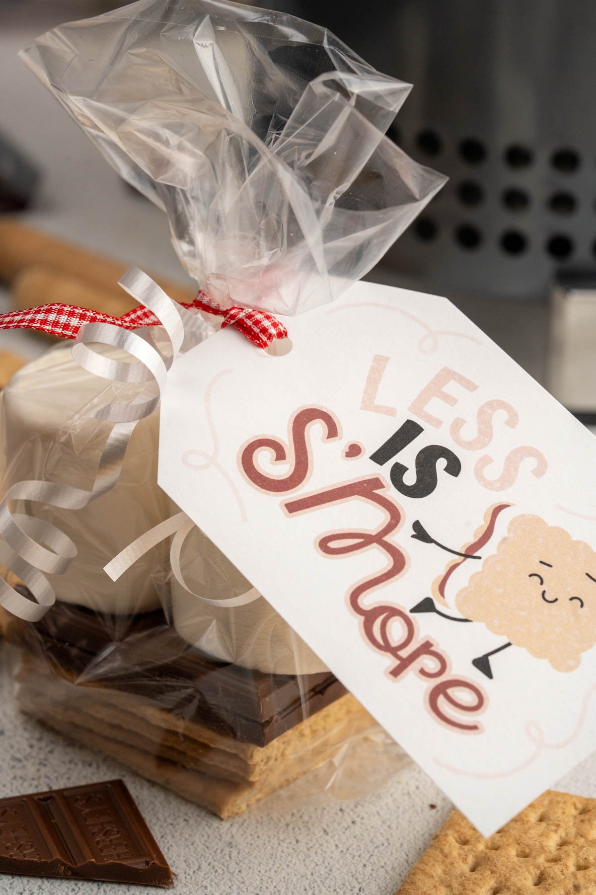 "Less is S'more" gift tag attached with ribbon to a S'more edible gift kit.